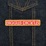 An embroidered rectangular patch with the text 'BIGGUS DICKUS' in cream lettering on a red background, bordered in gold.