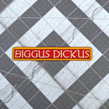 An embroidered rectangular patch with the text 'BIGGUS DICKUS' in cream lettering on a red background, bordered in gold.