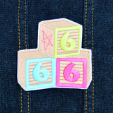 An embroidered patch resembling three children's building blocks showing the number six in three different colors.