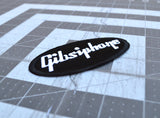 Close up detail of an oval-shaped black embroidered patch with the word 'Gibsiphone' stitched in white, resembling the logo for Gibson and Epiphone guitars.