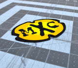 Close up detail of a black and yellow oval-shaped logo patch for the comedy tv show MXC.