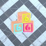 An embroidered patch resembling three children's building blocks showing the number six in three different colors.