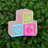 An embroidered patch resembling three children's building blocks showing the number six in three different colors.