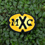 A black and yellow oval-shaped logo patch for the comedy tv show MXC.