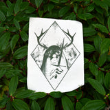 A rectangular off-white fabric patch featuring a dark green graphic print of an antlered figure holding a dagger, surrounded by a diamond border.