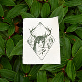 A rectangular off-white fabric patch featuring a dark green graphic print of an antlered figure holding a dagger, surrounded by a diamond border.