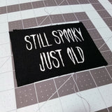 White on black screen printed canvas patch that says still spooky, just old.