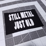 White on black screen printed canvas patch that says still metal, just old.