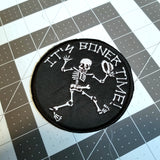 A round embroidered patch of a dancing skeleton that says, 'It's boner time!'