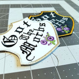 A pair of emblem-shaped embroidered patches with purple flowers and the words Got the Morbs in old english lettering. One is white with a silver border, the other black with a gold border.
