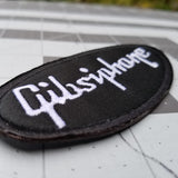 White on black Gibsiphone embroidered patch, a parody mashup of Gibson and Epiphone guitars.